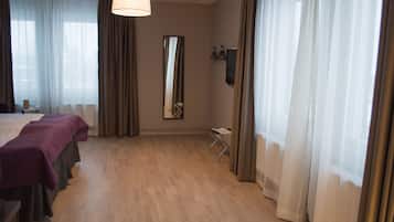 Hotellihuone, jossa on suuri sänky, työpöytä, tuoli, peili ja ikkuna, jossa on verhot.