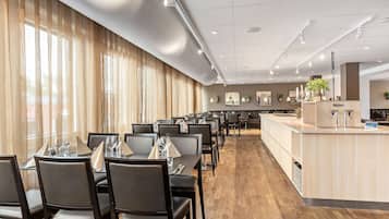 Une salle à manger d’hôtel avec des tables dressées pour le service, un point d’eau et un long comptoir agrémenté d’un miroir et de plantes.