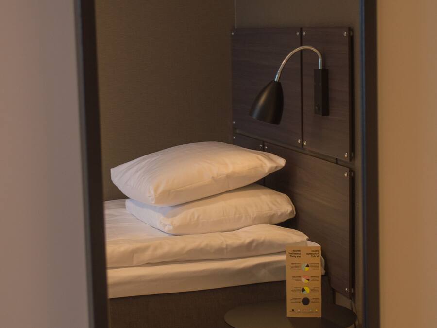 A compact room with a bed, a small table, and a wall-mounted lamp.