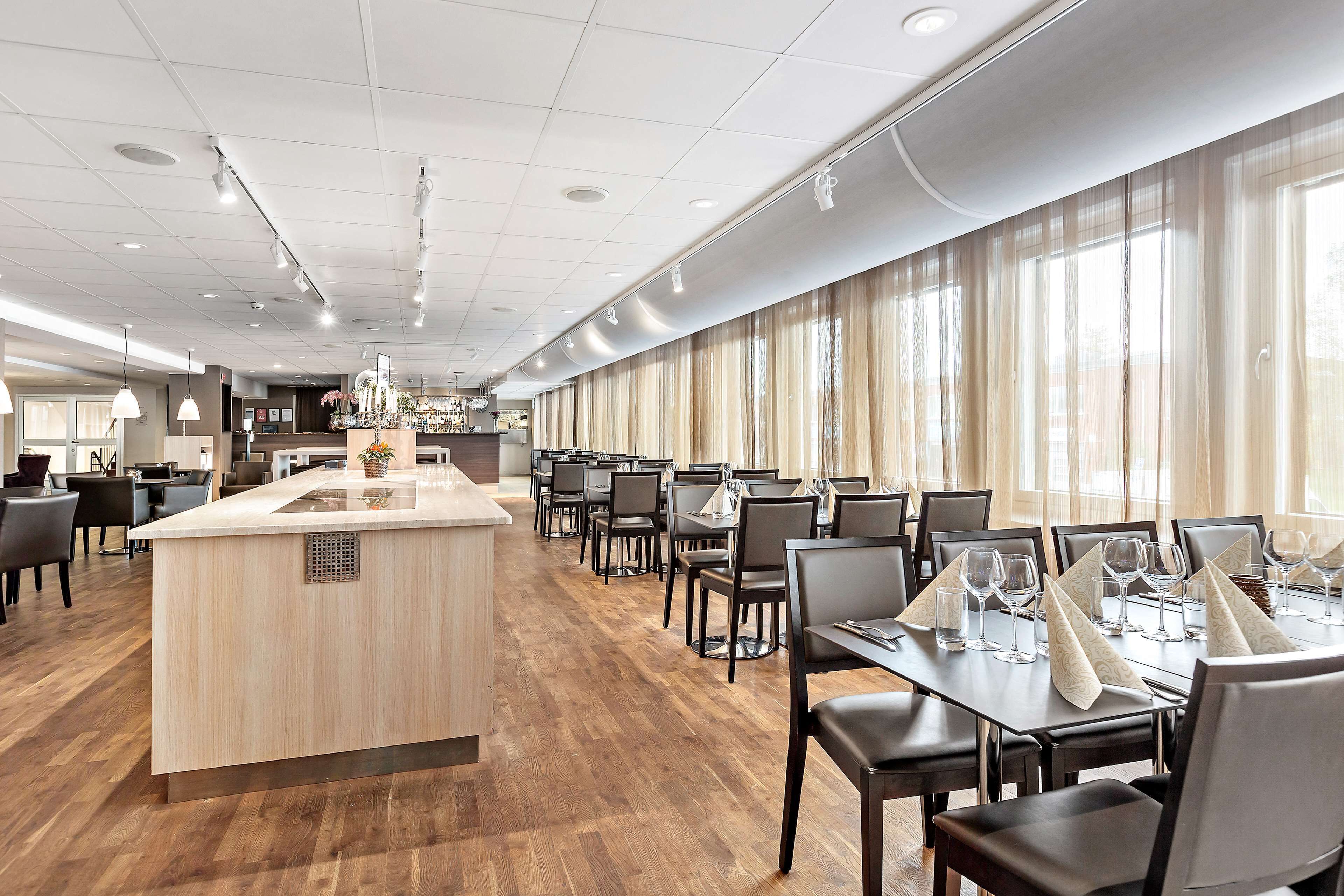 A modern dining area with a central island, long tables, and a view of the kitchen in the background.