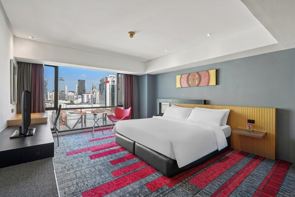 A modern hotel room with a large bed, a TV, a balcony with a city view, and a red and gray carpet. - BelAire Bangkok Sukhumvit (Bangkok)