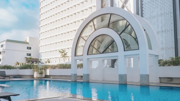 A modern hotel with a large pool, a covered seating area, and a distinctive arched glass structure. - BelAire Bangkok Sukhumvit (Bangkok)