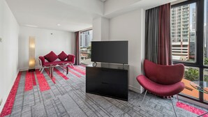 A modern hotel room with a large window, a flat-screen TV, a red chair, and a red sofa. - BelAire Bangkok Sukhumvit (Bangkok)