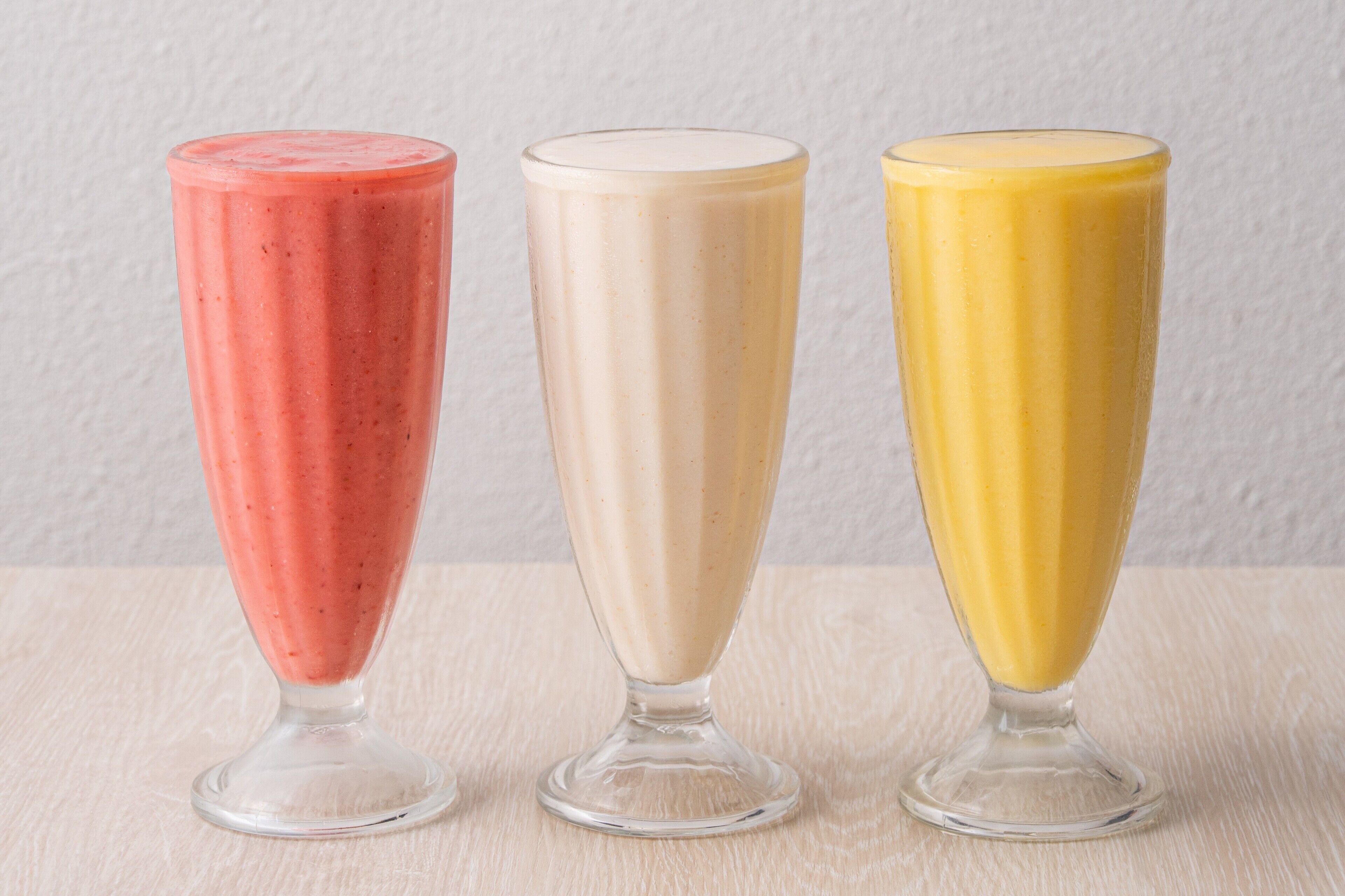 Three tall glasses of different colored smoothies on a wooden surface.