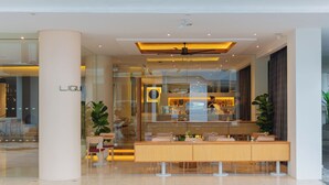 A modern hotel lobby with a reception desk, seating area, and a large glass window. - BelAire Bangkok Sukhumvit (Bangkok)