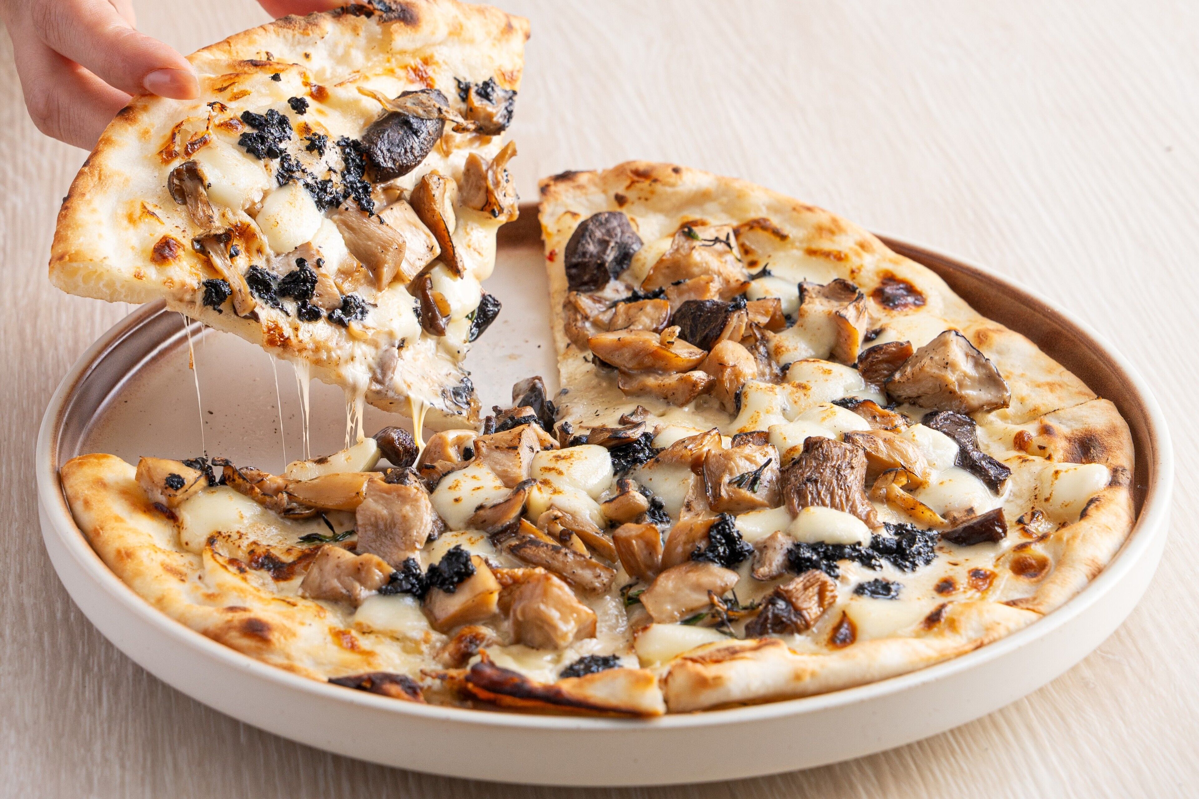 A pizza with various toppings being lifted from a tray.