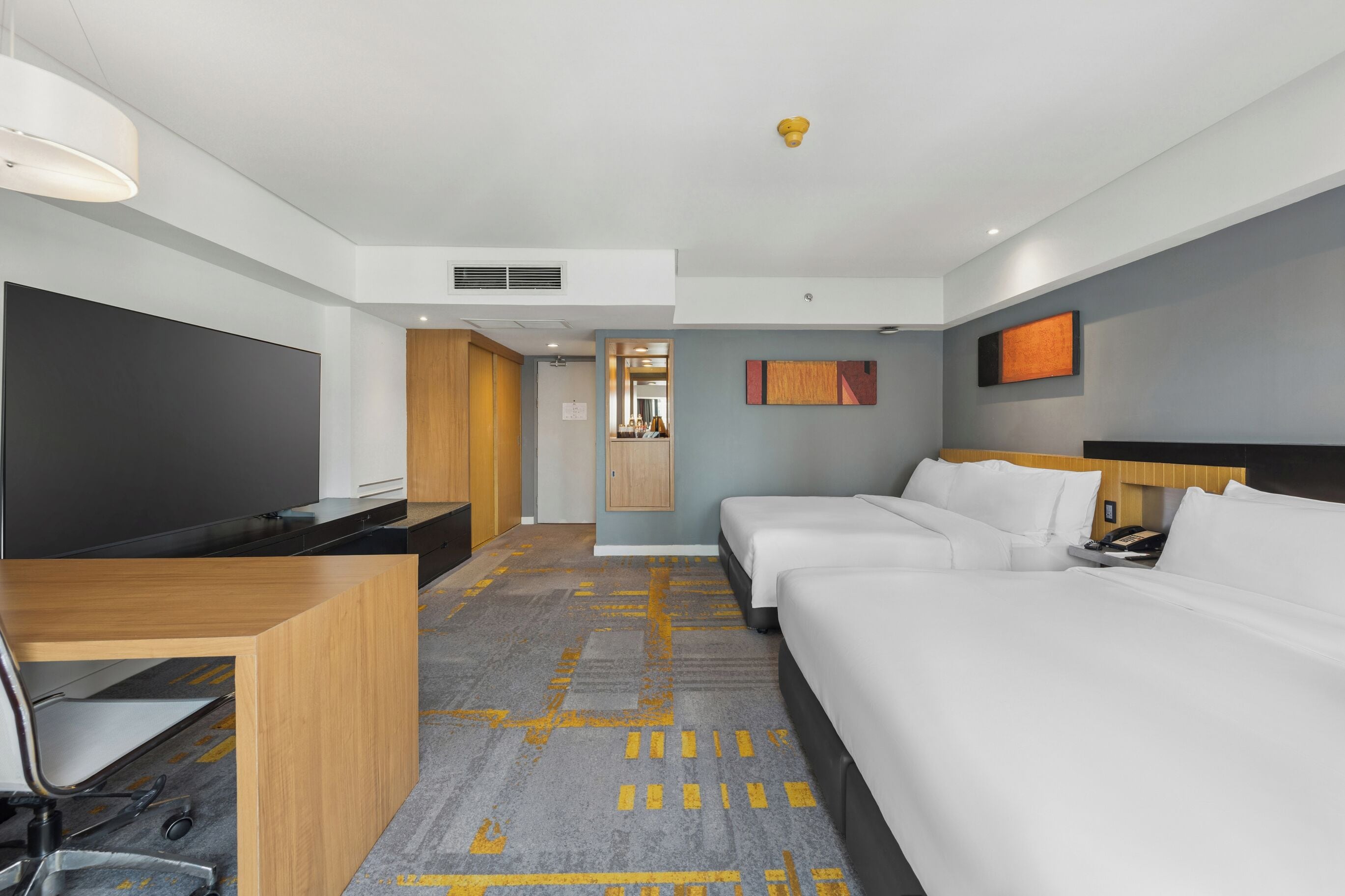 A hotel room with a bed, a desk, a TV, a wardrobe, and a bathroom visible through an open door.