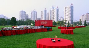 A spacious outdoor area with multiple round tables covered in red tablecloths, set up for an event. - Beijing Continental Grand Hotel (Beijing)