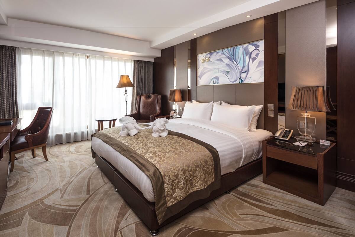 Une chambre d’hôtel avec un grand lit, deux chaises, un bureau et une table de chevet avec une lampe.