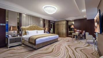 A spacious hotel room with a large bed, a chandelier, a desk with a chair, and a television.