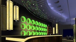 Un área de recepción moderna con un mostrador curvo de madera, exhibiciones circulares iluminadas en verde y un techo con iluminación empotrada.