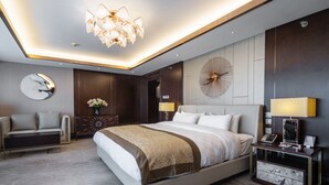 Una habitación de hotel moderna con una cama grande, un escritorio, una silla, una araña y un reloj de pared.