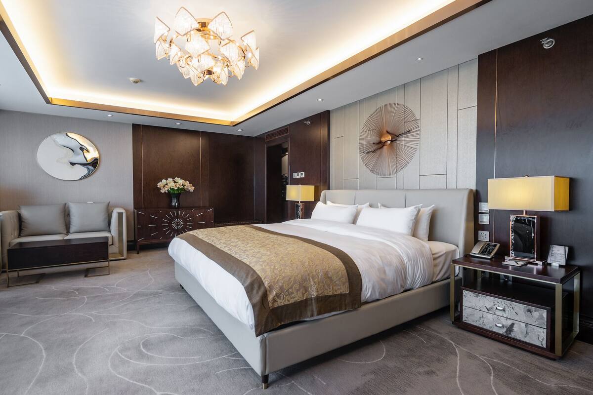 Une chambre d’hôtel moderne avec un grand lit, un bureau, une chaise, un lustre et une horloge murale.