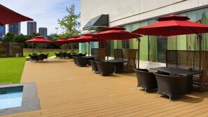 Un patio al aire libre con piso de madera, mobiliario de mimbre negro y sombrillas rojas.