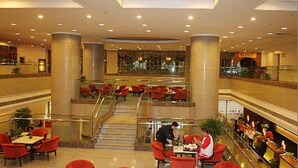 Un hall de hotel amplio con varias zonas de restauración, una escalera central y un mostrador de recepción.