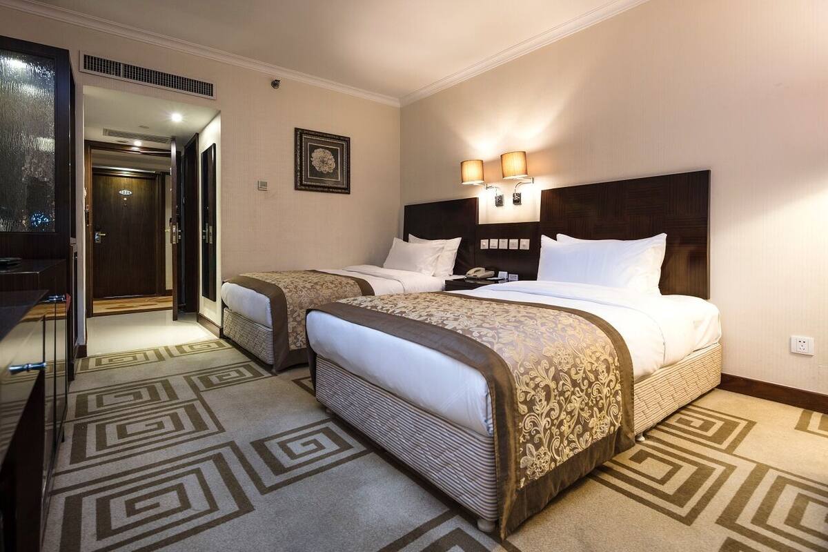 Une chambre d’hôtel avec deux lits, un grand miroir et une moquette à motifs.