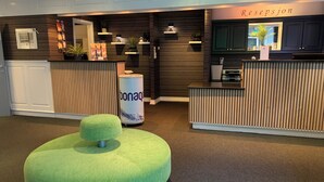Un espace d’accueil avec un banc recouvert d’un tissu vert, un présentoir cylindrique de la marque « bonaq » et une enseigne « Resepsjon » au-dessus du comptoir d’accueil.