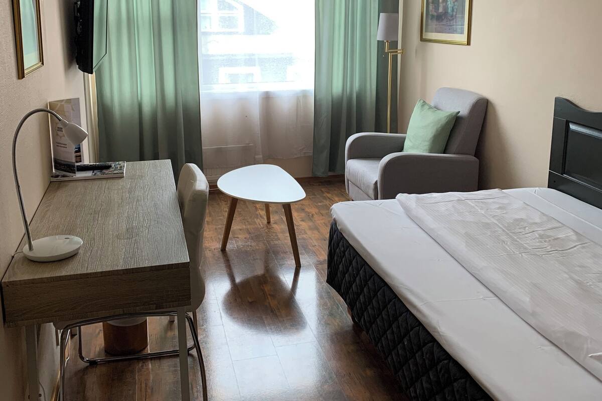 A hotel room with a bed, a desk with a chair, a small table, a sofa, and a TV.