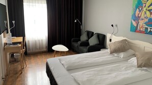 Une chambre d’hôtel avec un lit, un bureau, une chaise, une petite table et un tableau au mur.