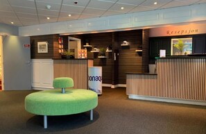 Un espace d’accueil avec un banc recouvert d’un tissu vert, un comptoir de réception et une enseigne sur laquelle on peut lire « Resepjon ».