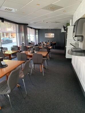 Relax in a spacious room with a large window offering a view of the street outside, a seating area with tables and chairs, and a coffee machine.
