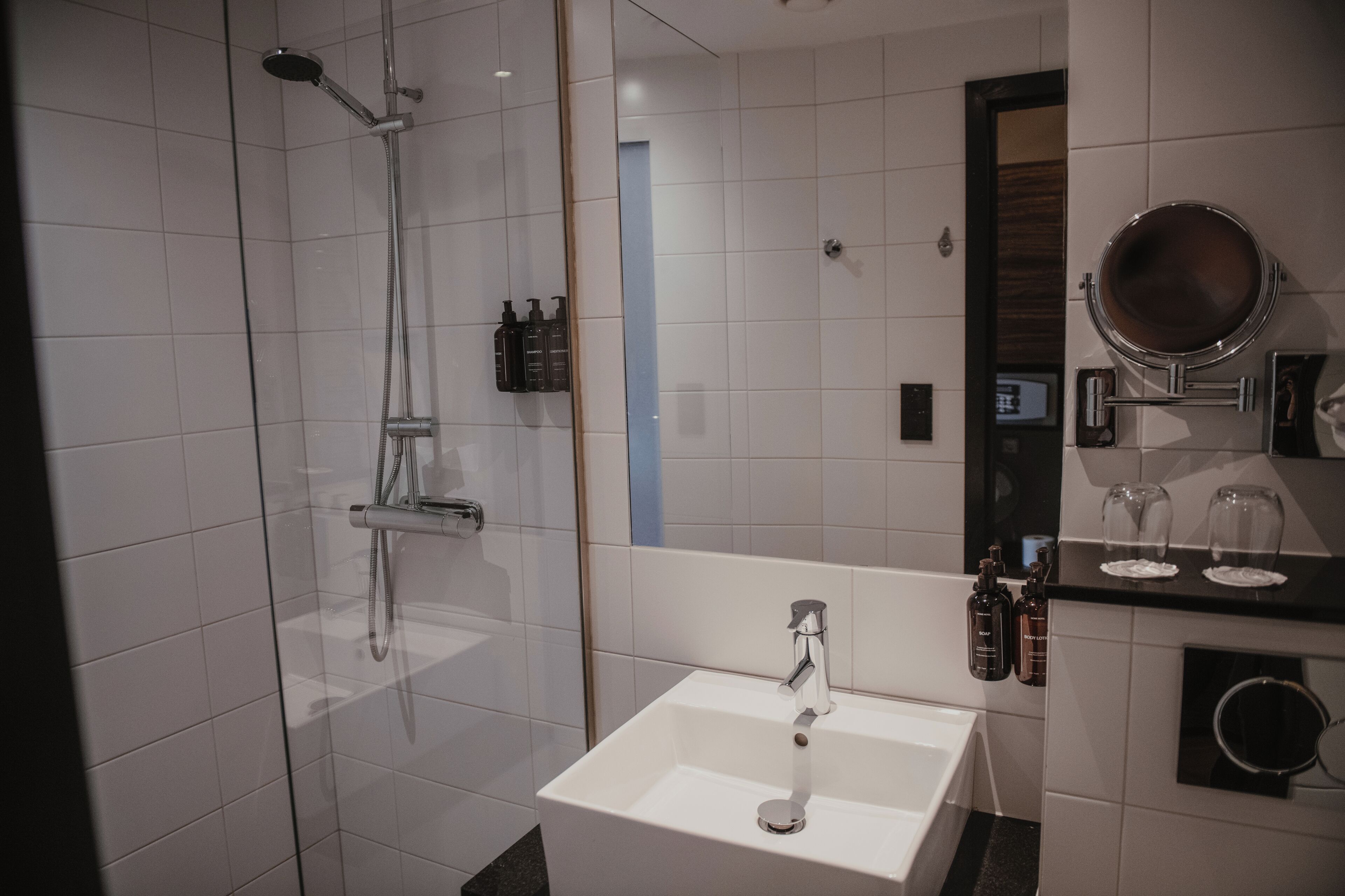 A modern bathroom with a glass-enclosed shower, a white sink, and a mirror with a round frame.
