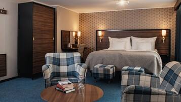 A hotel room with a large bed, two armchairs, a small table with books and a glass, and a wardrobe.