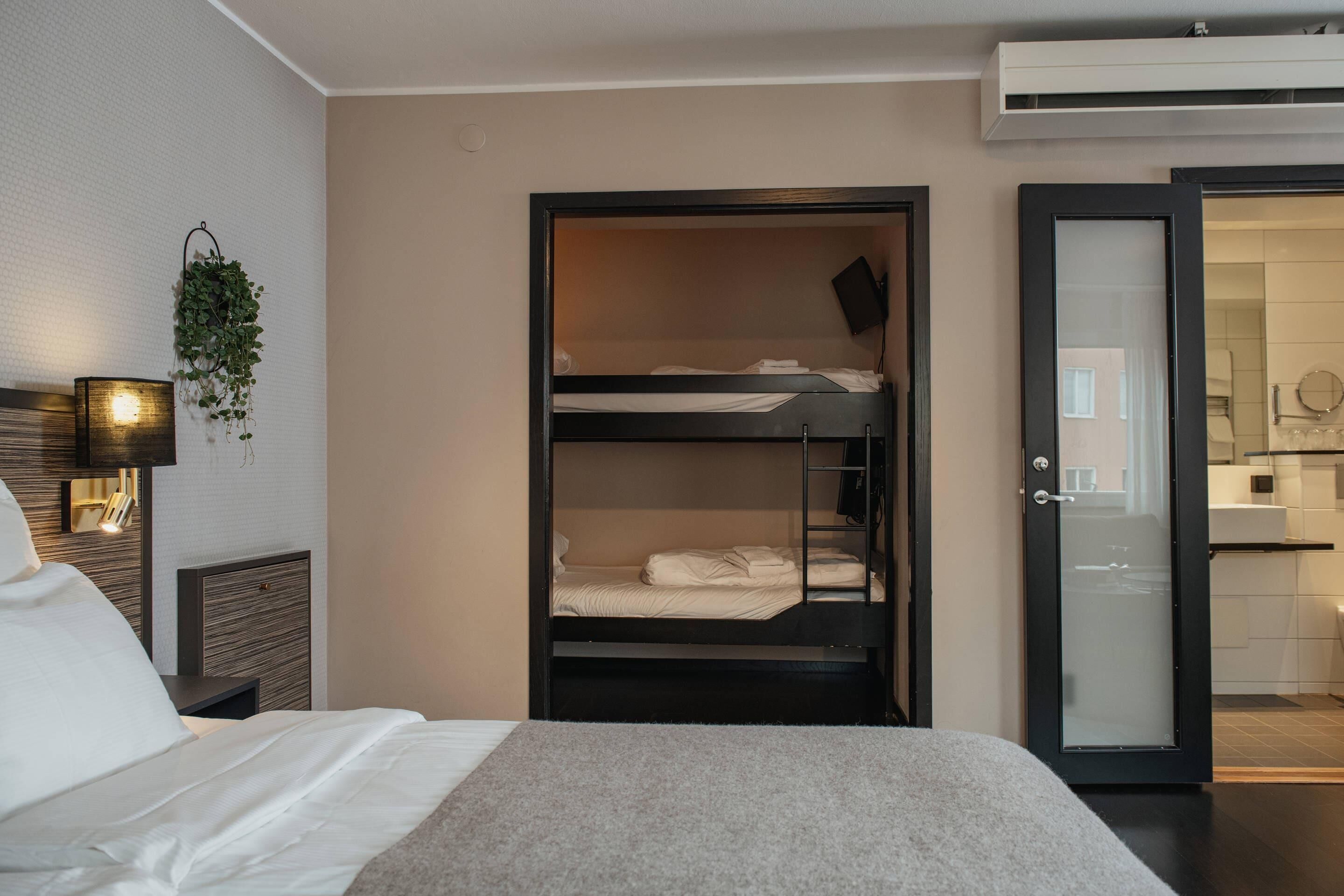 Une chambre d’hôtel avec un lit superposé, une table de chevet avec une lampe et une vue sur la salle de bain.