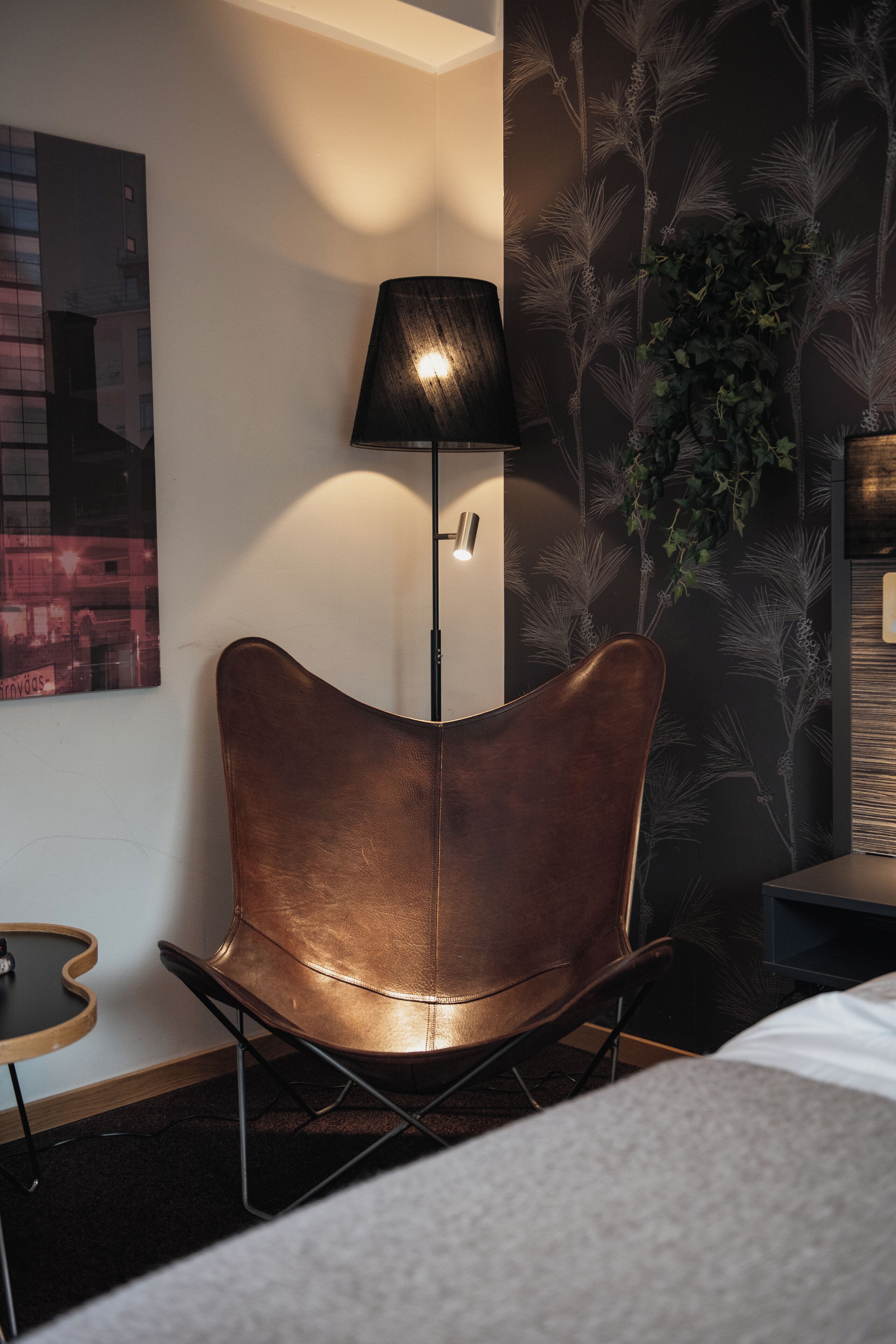 A modern room with a curved leather chair, a floor lamp, and a wall with a plant and a framed picture.