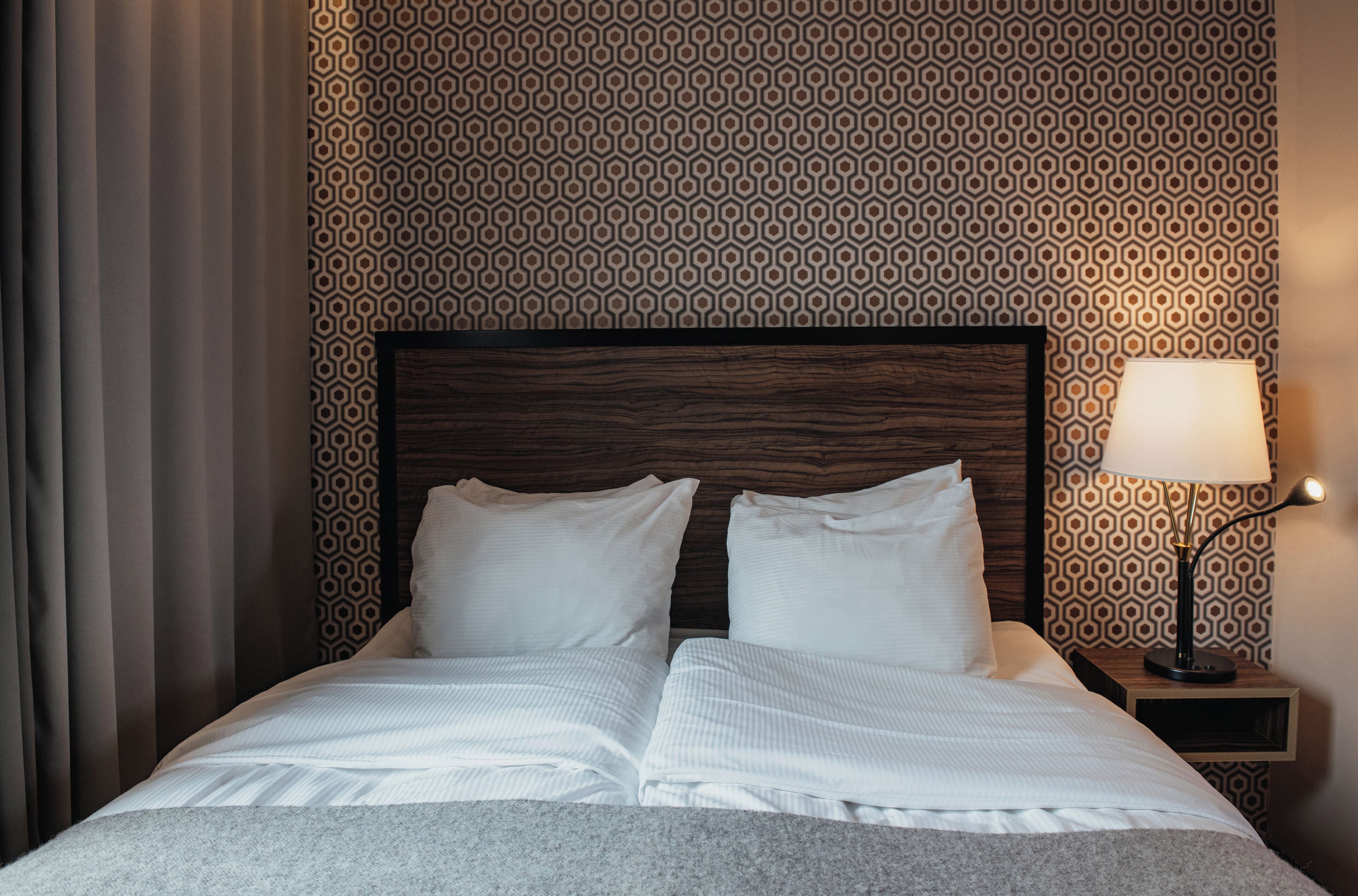 A neatly made bed with white linens, a wooden headboard, and a bedside lamp on a nightstand.
