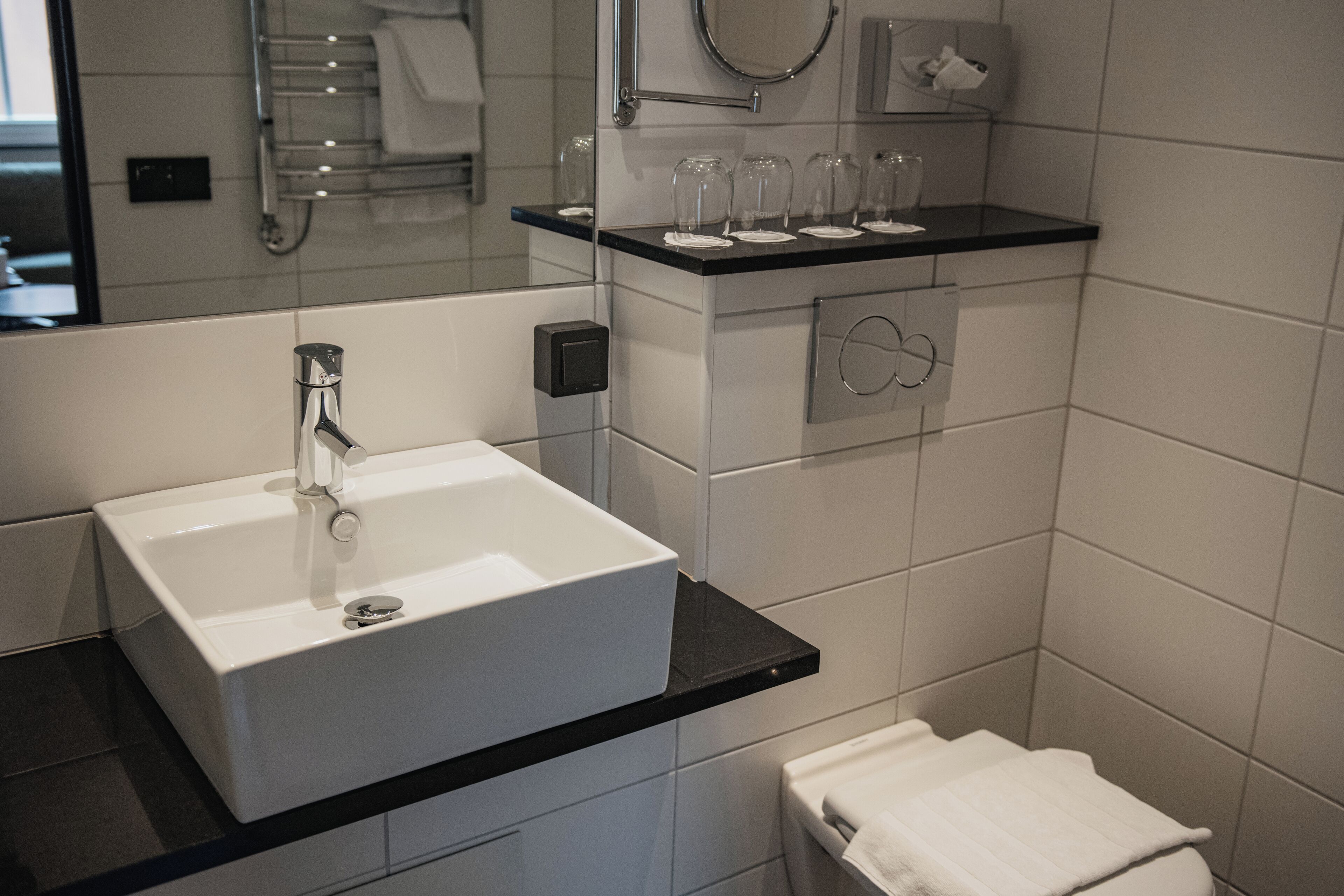 A modern bathroom with a white sink, black countertop, and a towel rack above the sink.