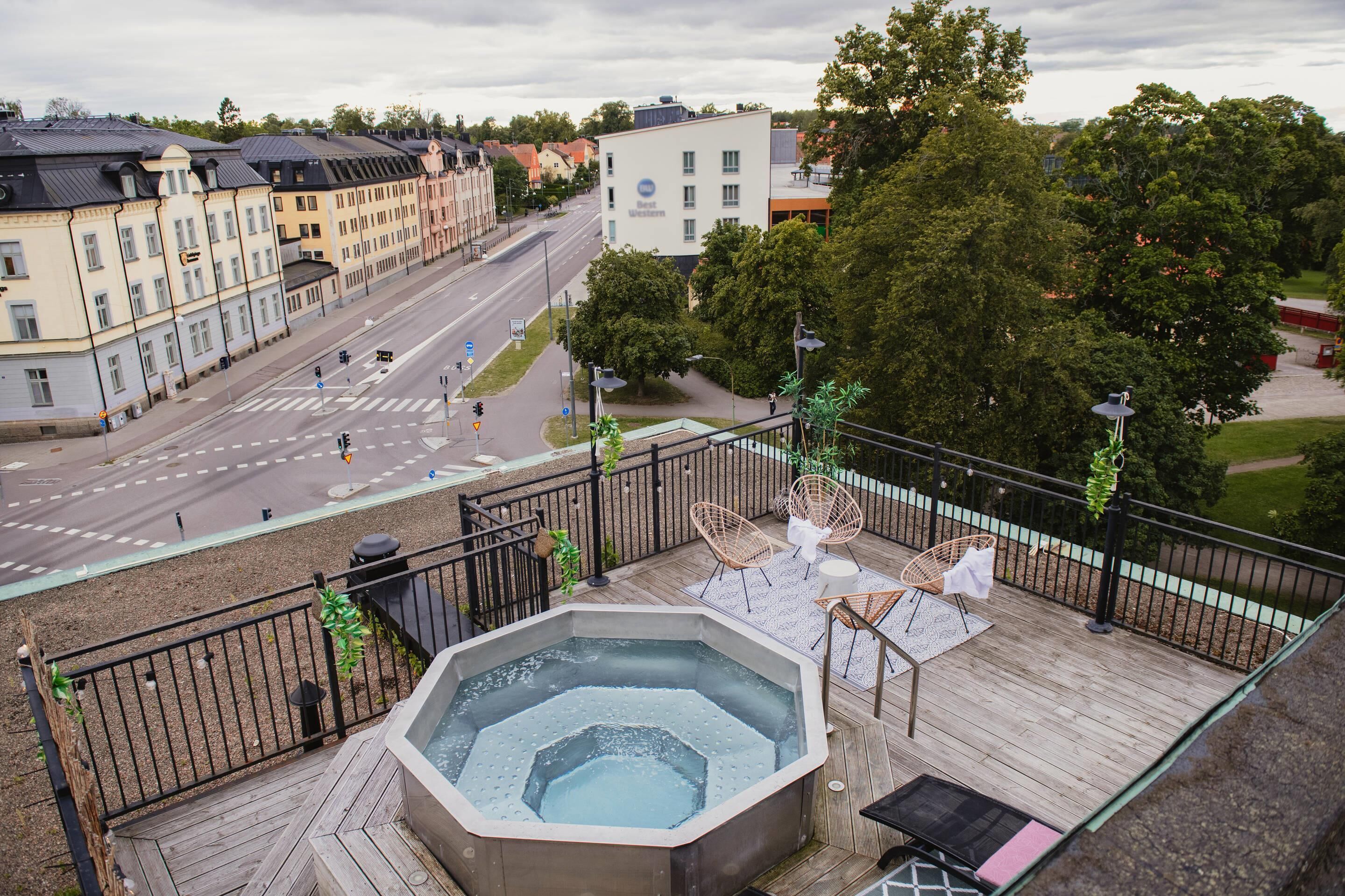 En takterrass med ett bubbelbad, utomhusmöbler och utsikt över stadsgatan.