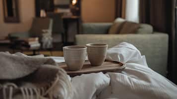 Cama bem arrumada com uma bandeja contendo duas xícaras de cerâmica, um sofá verde e uma cadeira em um quarto de hotel.