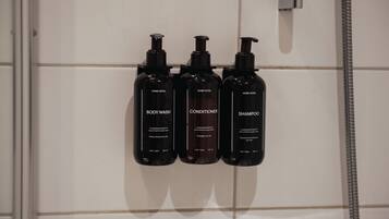 Drie zwarte flesjes toiletartikelen op een betegelde muur.