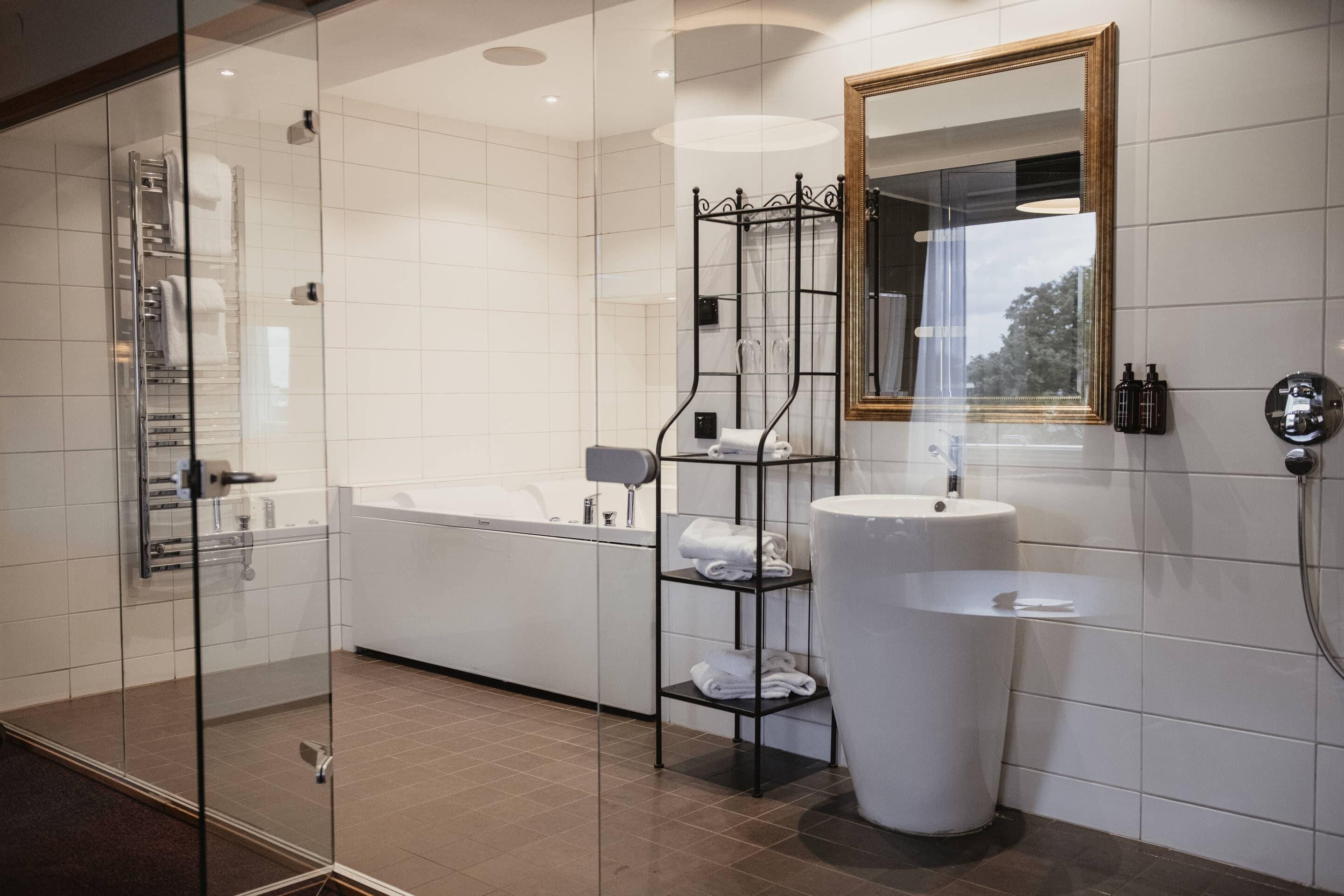 A modern bathroom with a glass shower enclosure, a bathtub, a large sink, and a mirror with a gold frame.