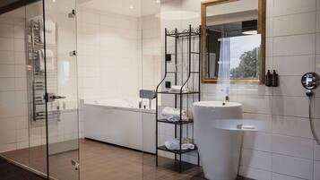 A modern bathroom with a glass shower enclosure, a bathtub, a large sink, and a mirror with a gold frame.