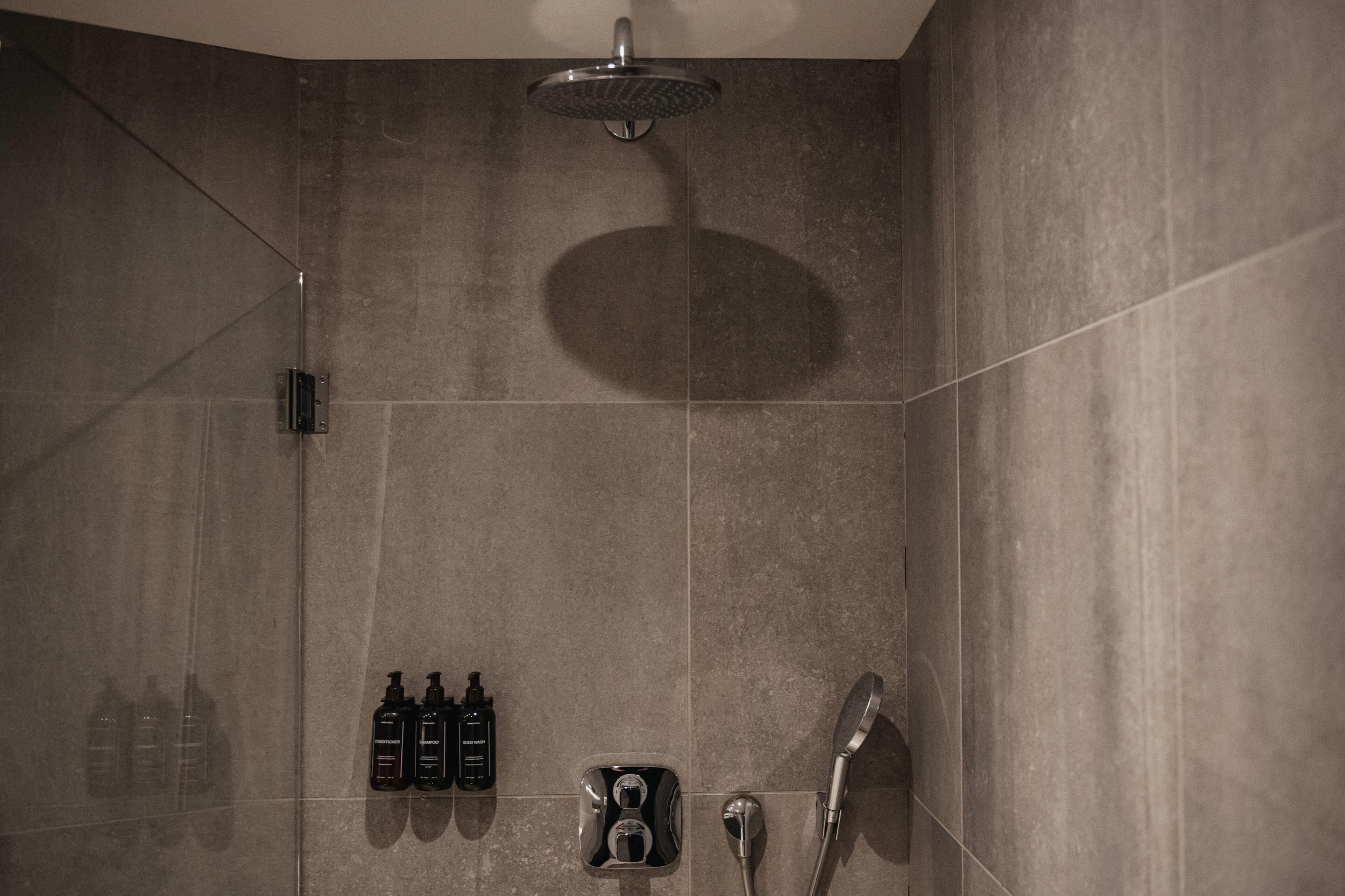 A modern shower area with a handheld showerhead, a wall-mounted control panel, and a set of toiletries including shampoo and conditioner.