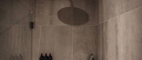 A modern shower area with a handheld showerhead, a wall-mounted control panel, and a set of toiletries including shampoo and conditioner.