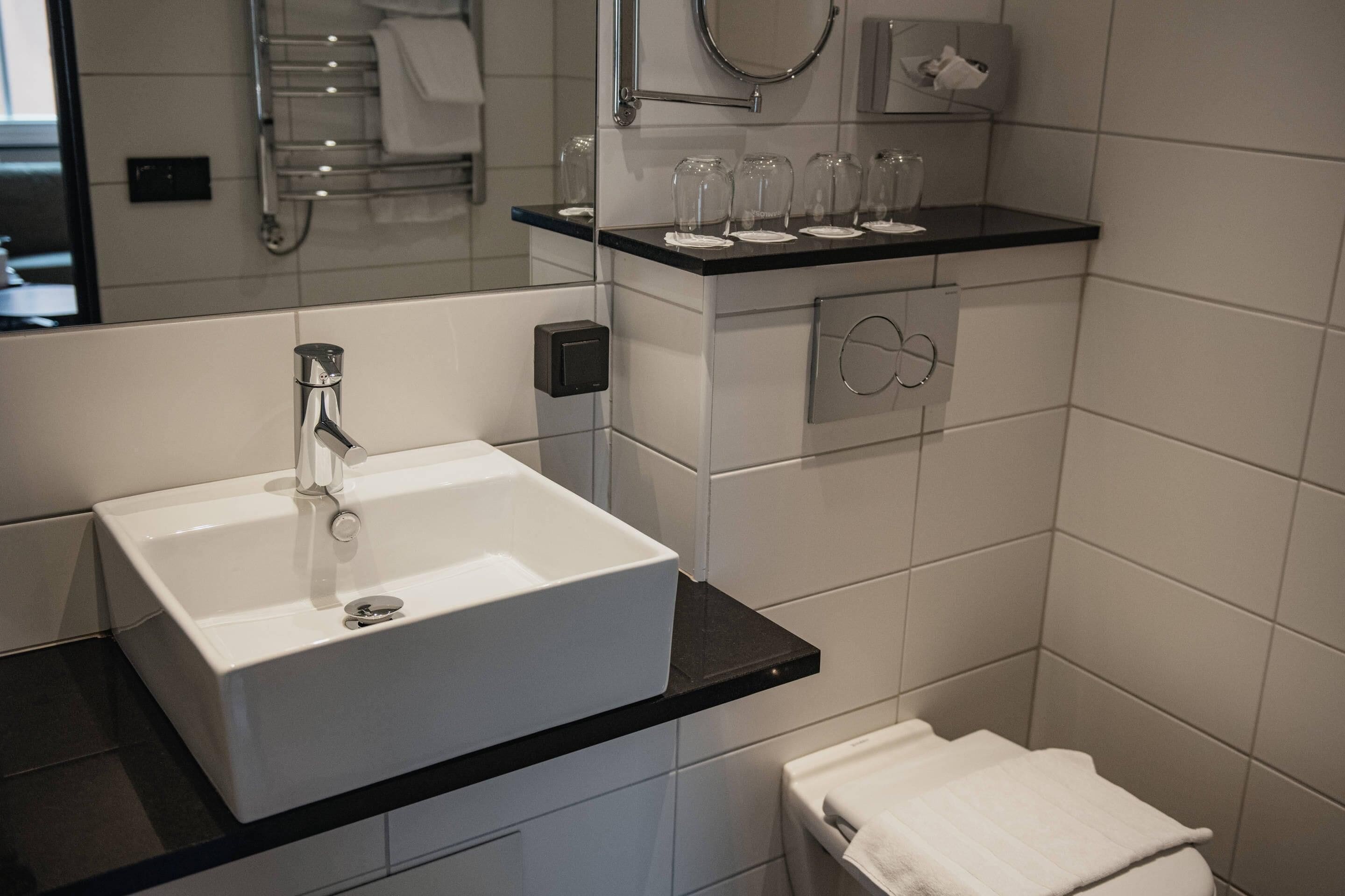 Un baño moderno con un lavamanos blanco, encimera negra y un perchero sobre el lavamanos.