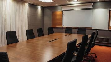 A conference room with a long wooden table, black chairs, a whiteboard, and a projector.