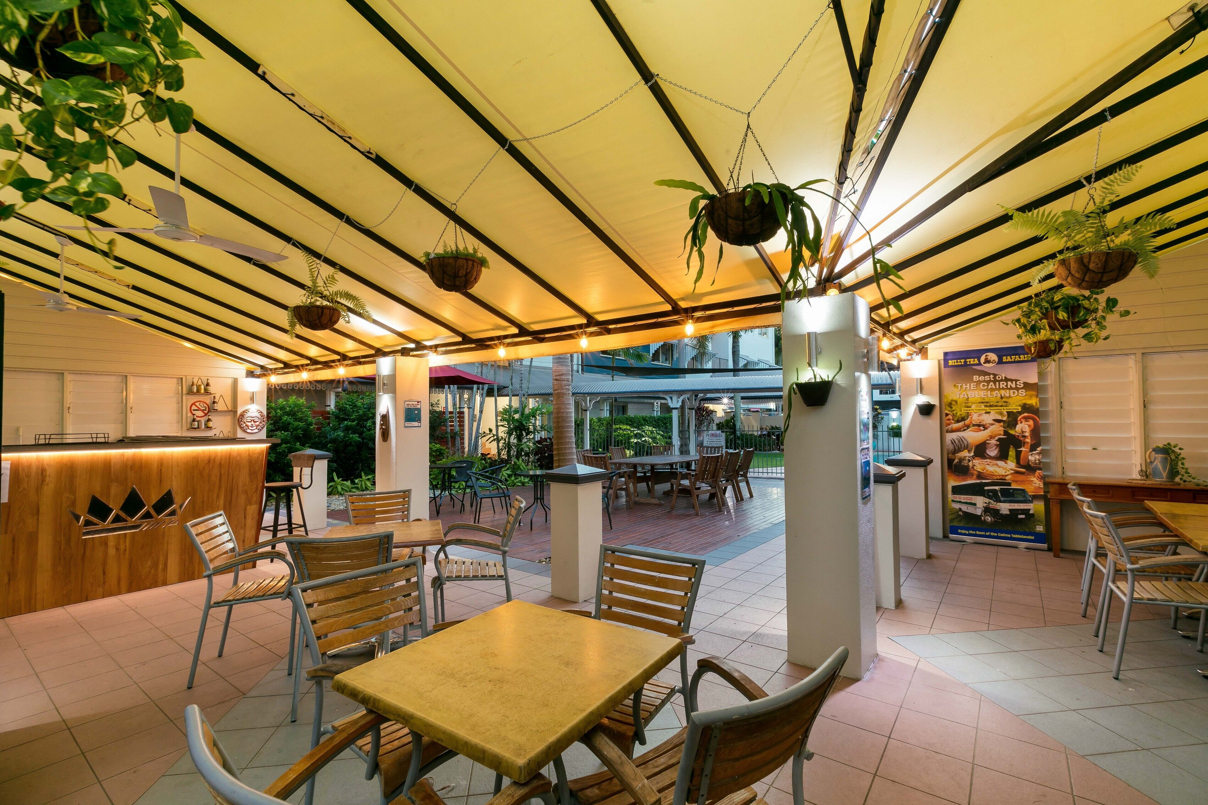 An indoor cafe with wooden tables and chairs, hanging plants, and a tiled floor.