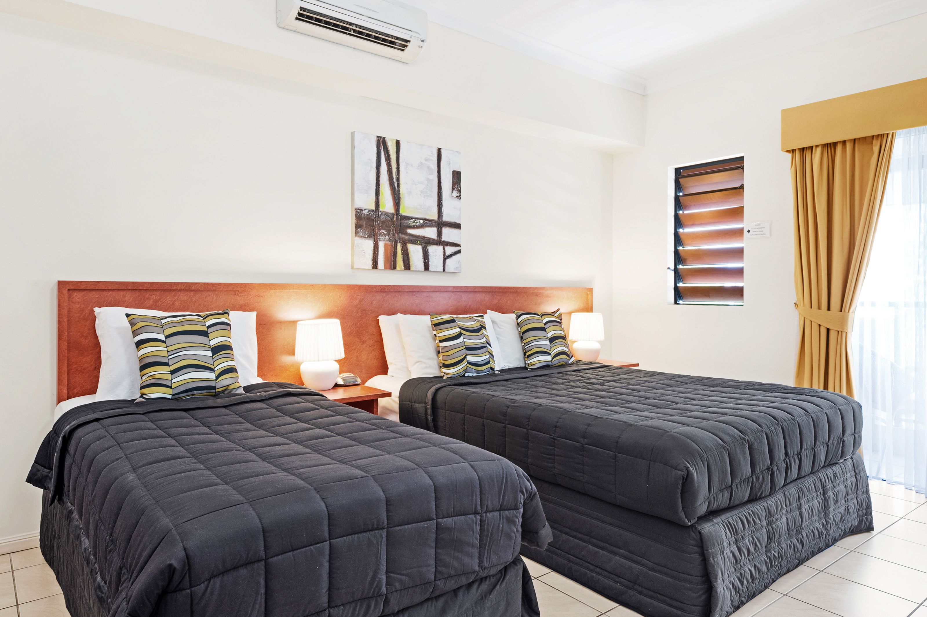 Ein Hotelzimmer mit zwei Betten, einem Holzkopfteil, gestreiften Kissen, Nachttischlampen und einem großen, abstrakten Gemälde an der Wand.