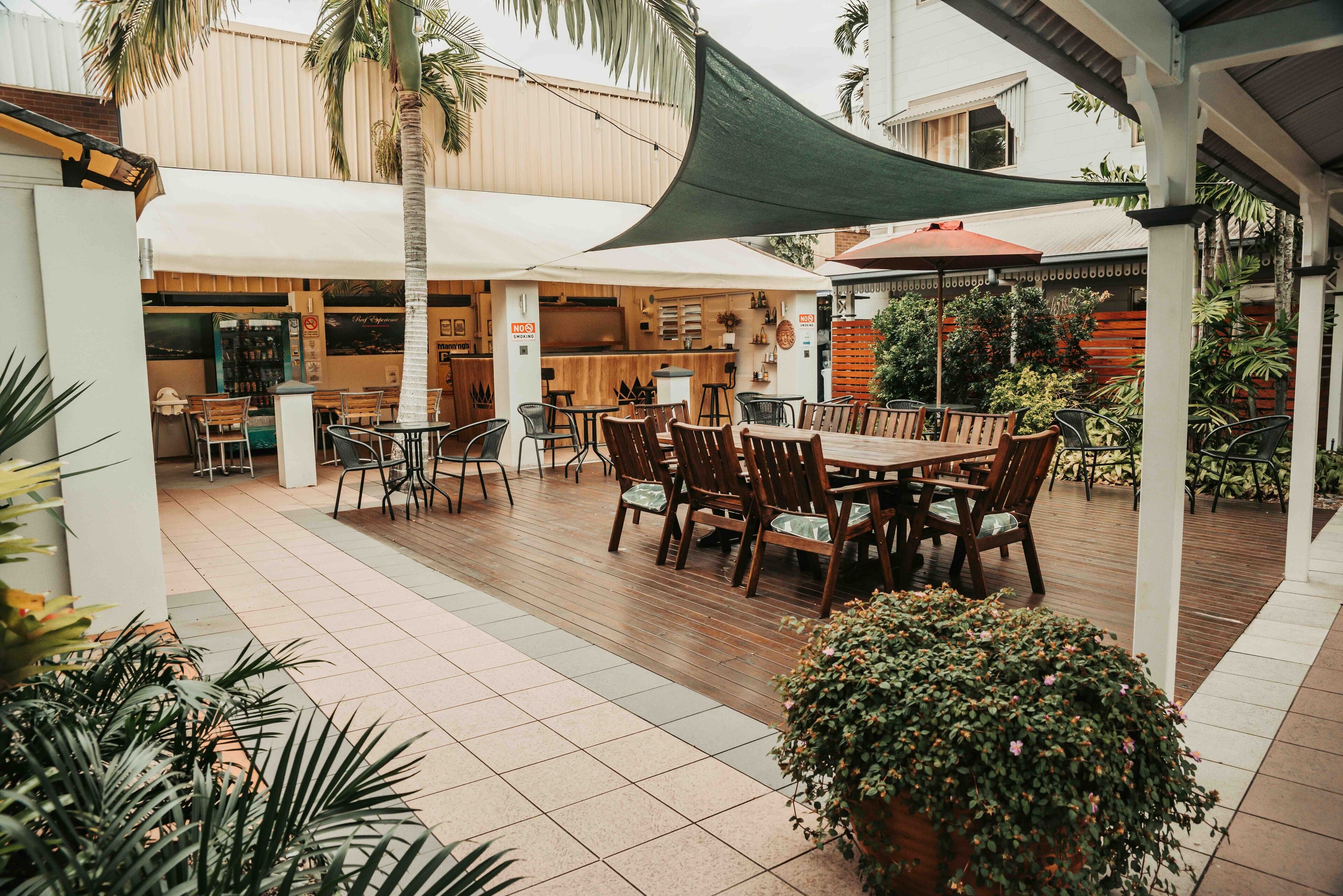 An outdoor patio area with wooden tables and chairs, a bar area, and potted plants.