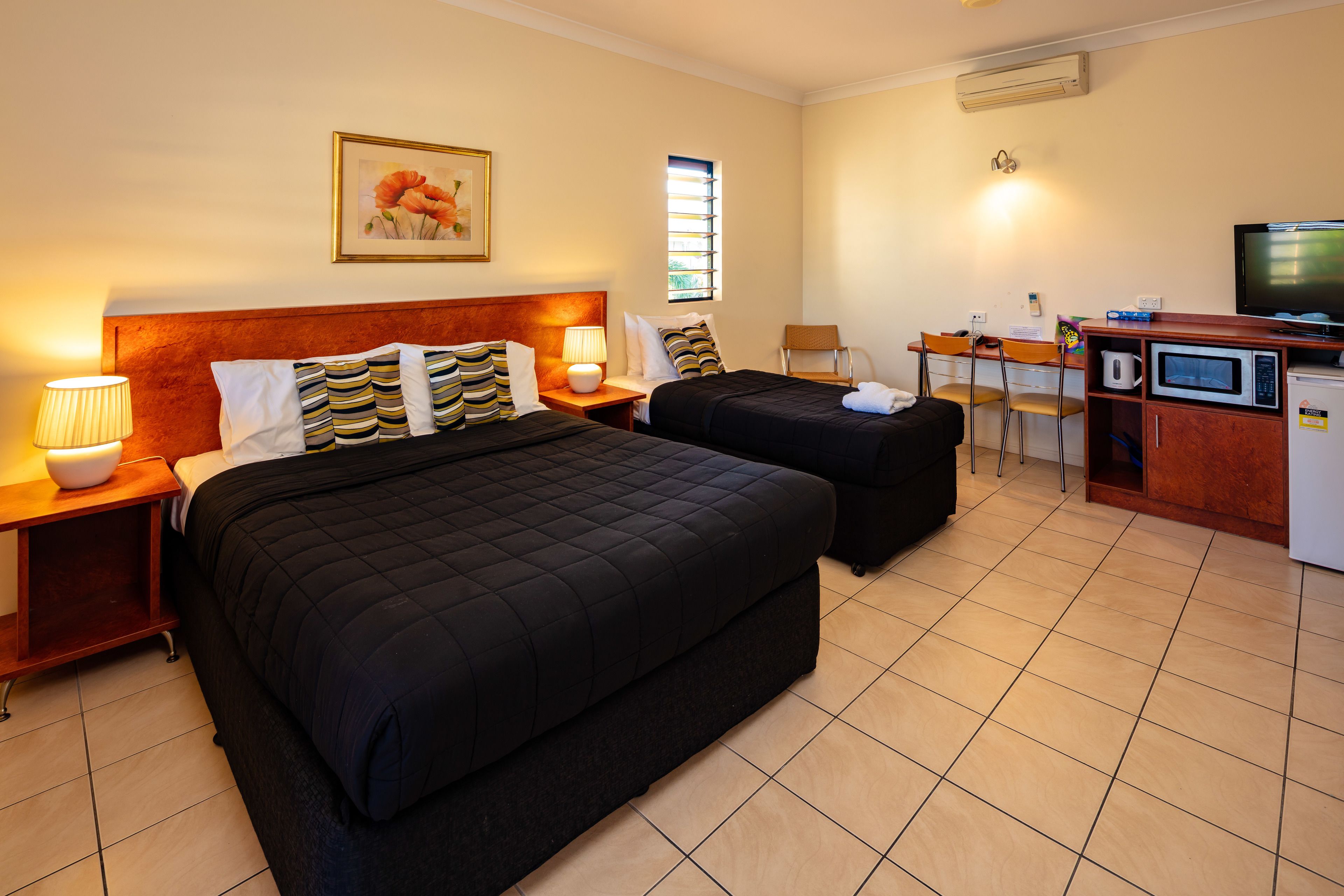A hotel room with two beds, a desk with a chair, a microwave, and a television.