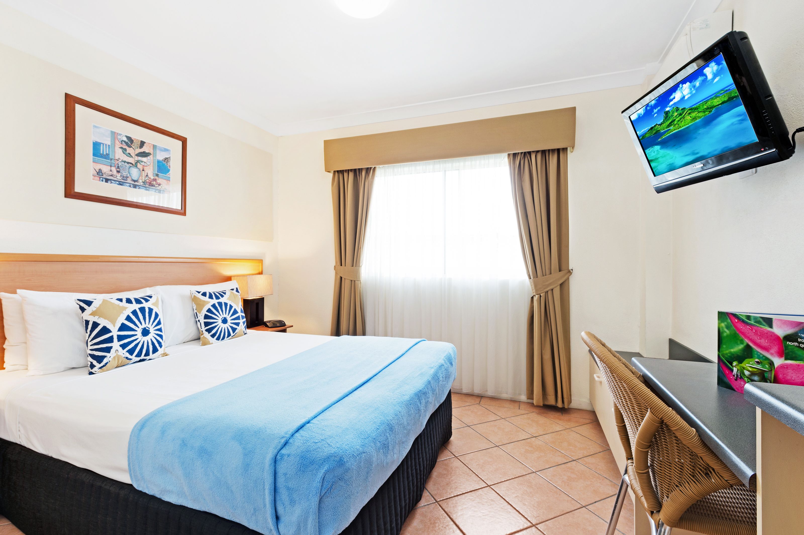 A hotel room with a bed, a desk, a television, and a window with curtains.