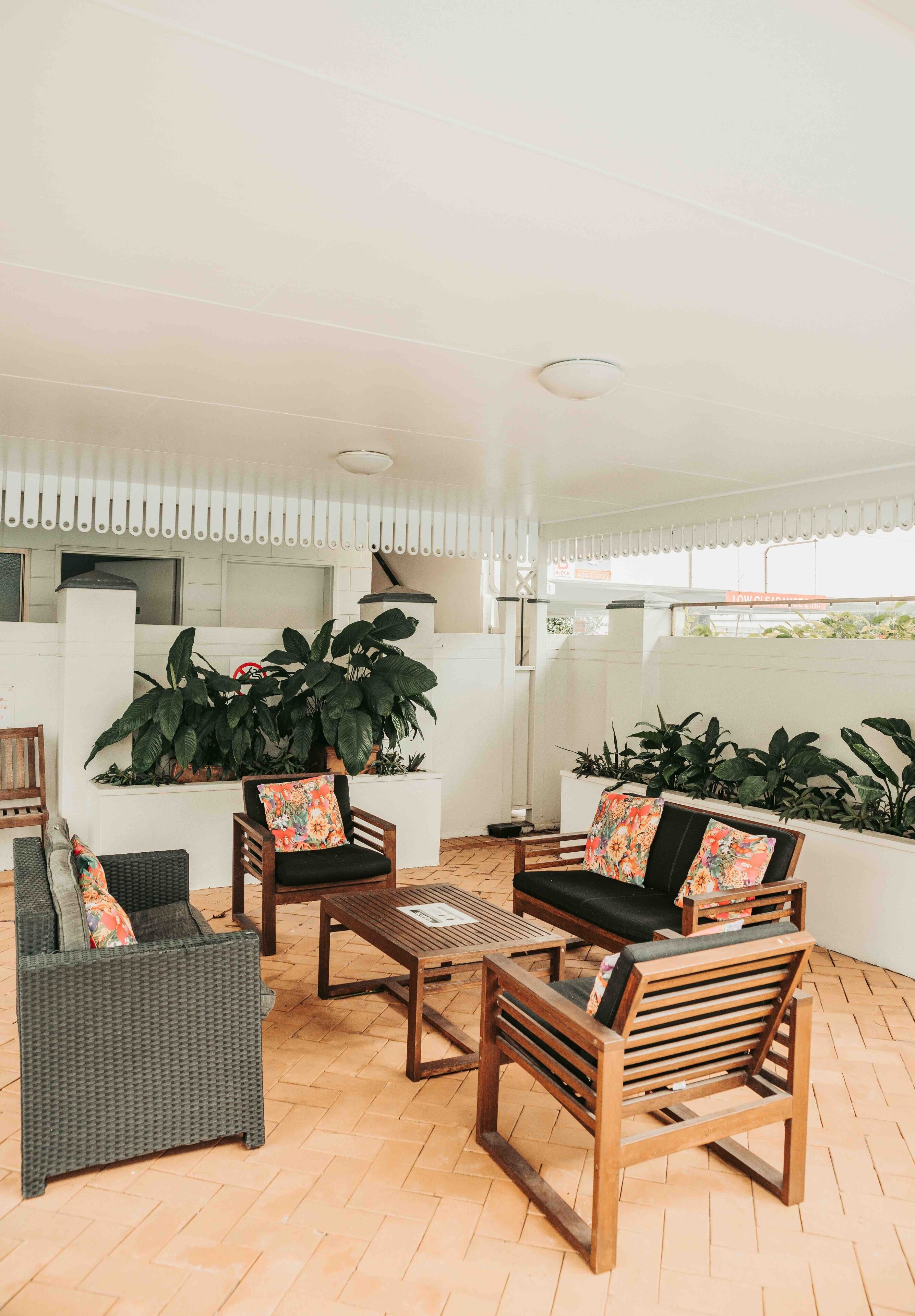 A modern outdoor seating area with wicker furniture and wooden chairs, surrounded by large potted plants.