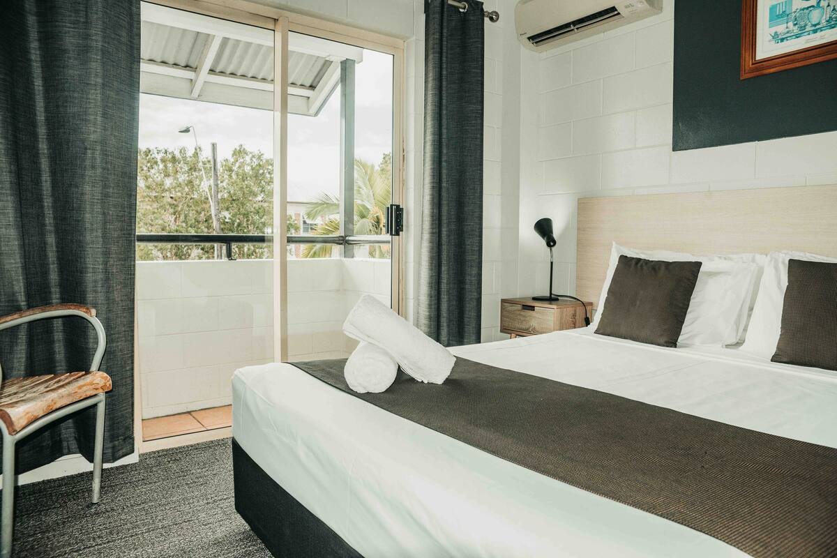 Une chambre d’hôtel avec un lit, une chaise, une table de chevet et une vue sur l’extérieur.