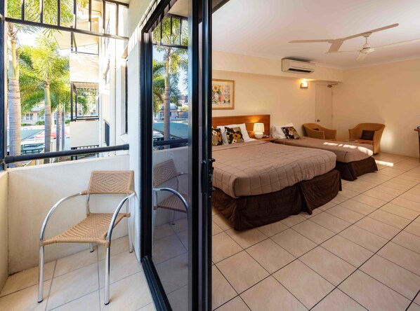 Une chambre d’hôtel avec deux lits, un balcon doté de fauteuils en osier et une vue sur les palmiers.