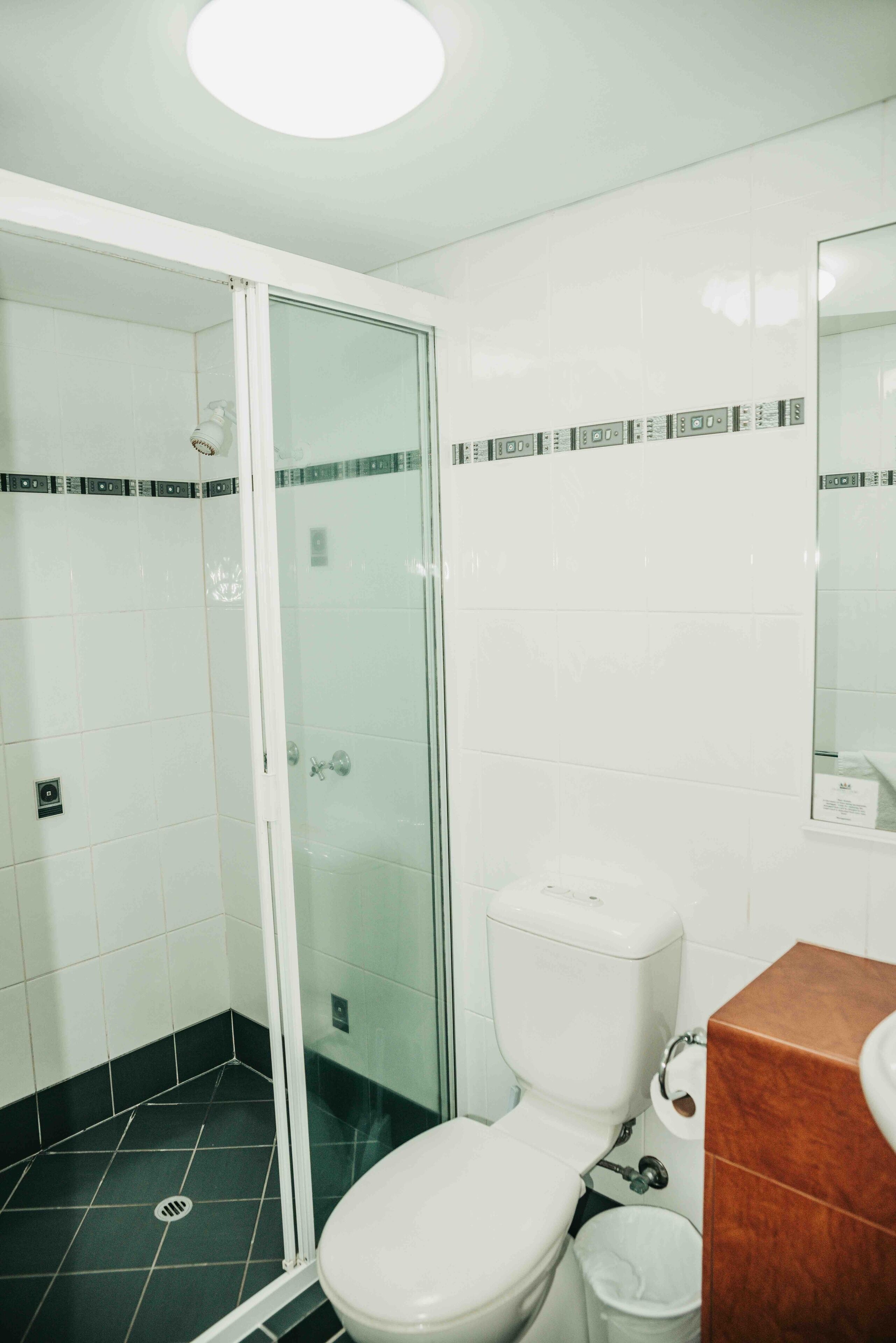Un baño con cabina de ducha de vidrio, inodoro blanco y lavamanos marrón.