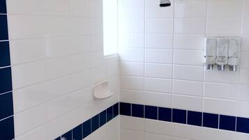 A bathroom with white and blue tiles, a shower, a window, and a soap dispenser.